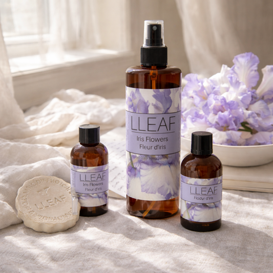 LLeaf Iris Flowers products including bottles and a bar of soap on a soft surface with flowers in the background.