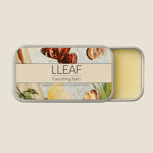 A silver metal tin of LLEAF Everything Balm, shown open to reveal the pale yellow balm inside. The lid features a decorative label with illustrations of butterflies, leaves, and flowers, and a beige banner across the middle with the brand name 'LLEAF' and product name 'Everything Balm'.