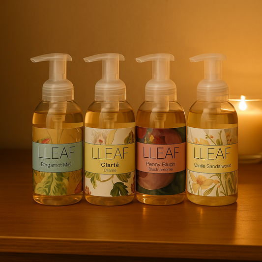 Four LLEAF soap bottles on a wooden surface with a candle in the background.